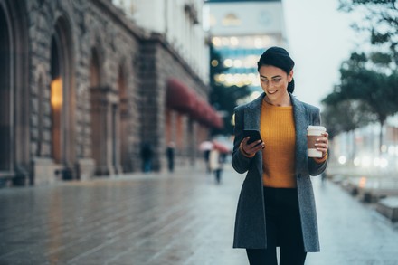 Woman walking in the street and drinking coffee with her smartphone in her hand